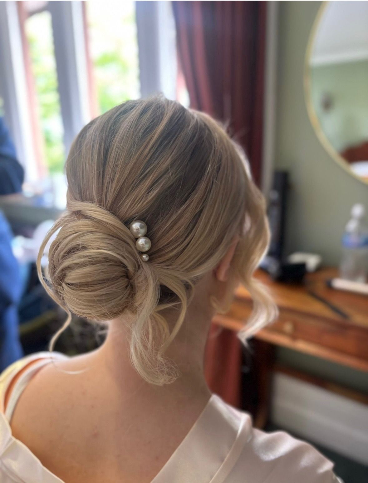 Low blonde bridal bun finished with pearl pins, seen from behind