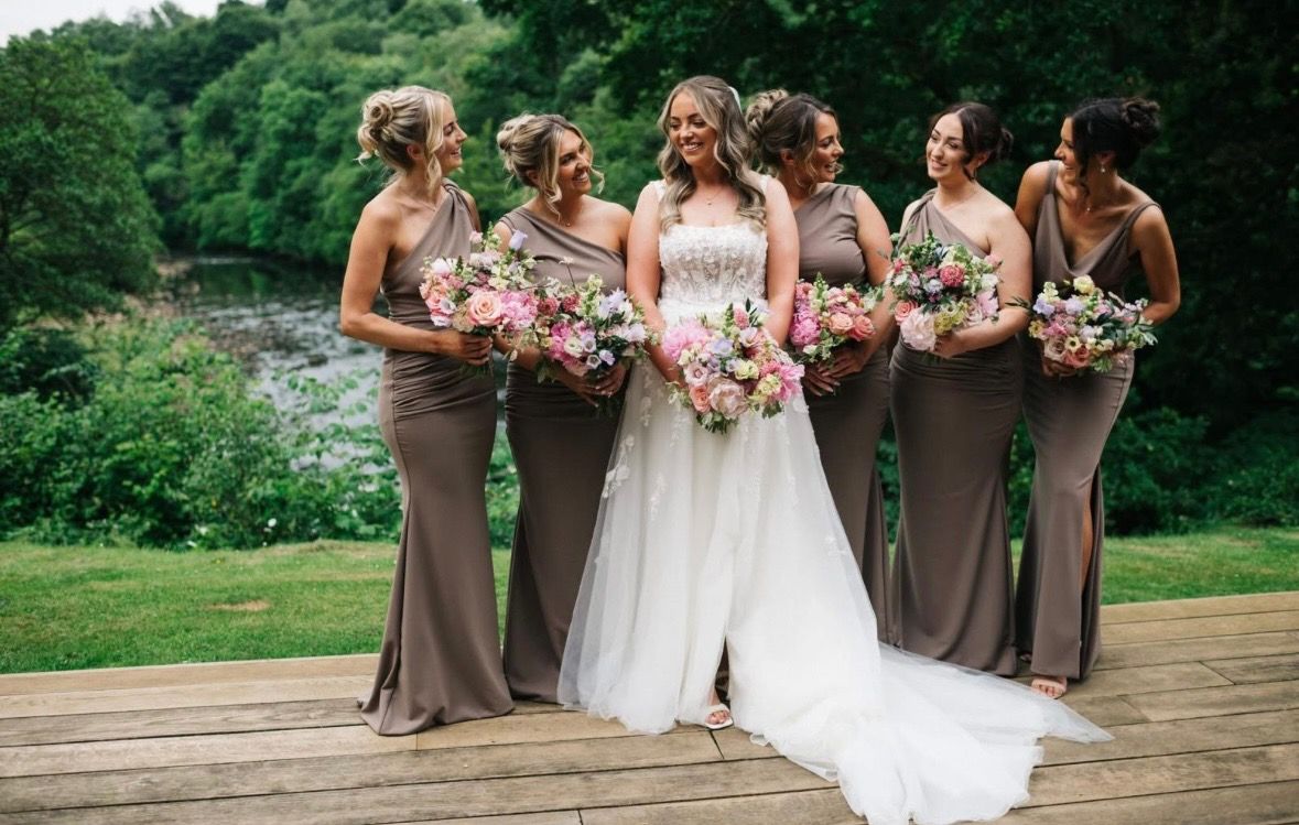 Bride with her bridesmaids in taupe dresses, holding bouquets outdoors