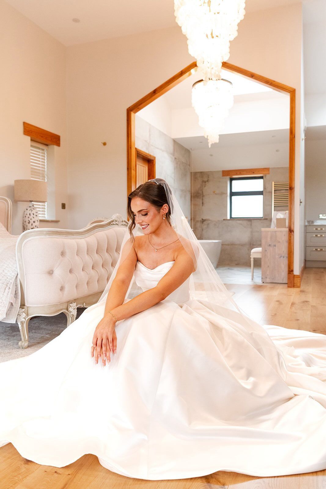 Bride in a full white gown sitting on a sofa in a bright, elegant room