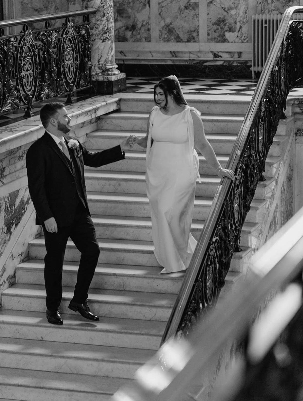 Black and white photo of a bride and groom walking down a grand marble staircase
